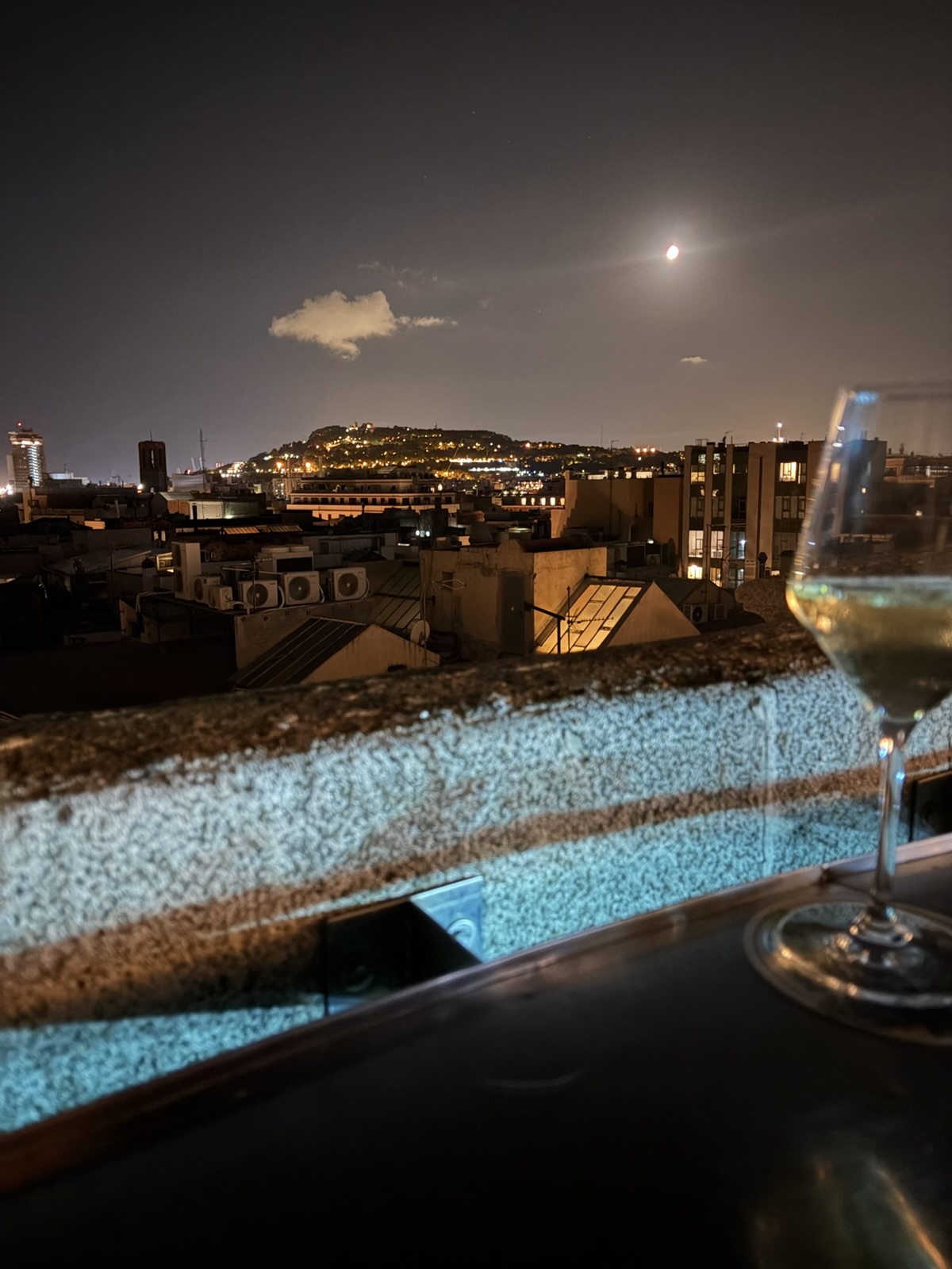Nächtlicher Blick über die Dächer einer Stadt, im Vordergrund ein Weinglas